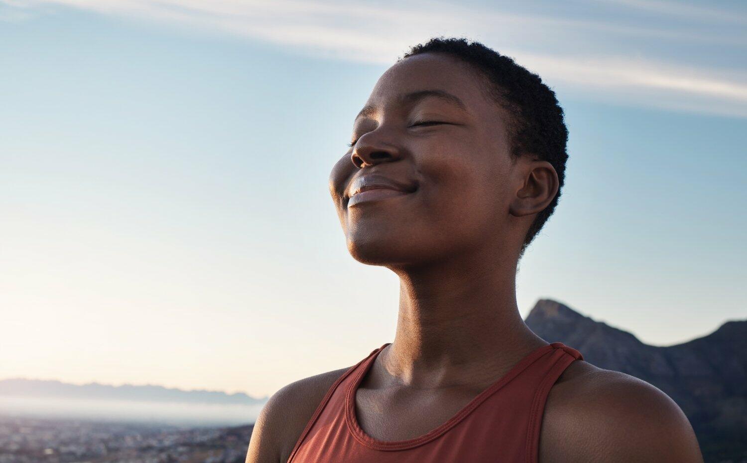 Fitness, calm and breathing of black woman outdoor in nature, mountains and blue sky background