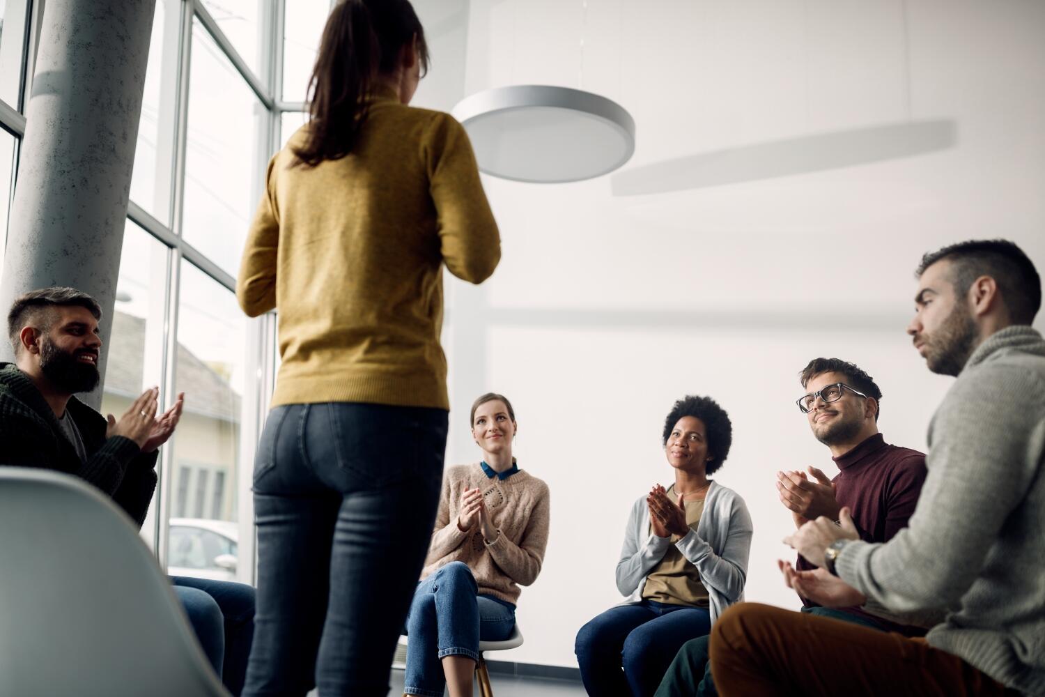 Low angle view of group therapy participants applauding to a woman during the meeting.