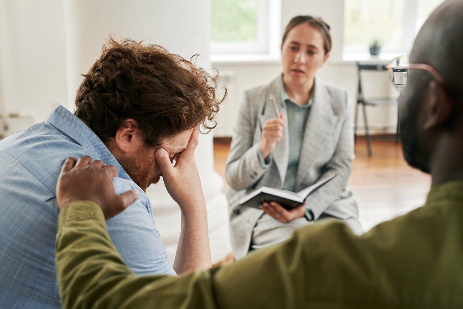Worried male patient keeping hand on head while black man comforting him (1)