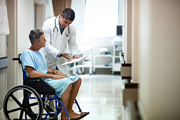 Shot of a doctor talking to a patient in a wheelchair in a hospital corridor
