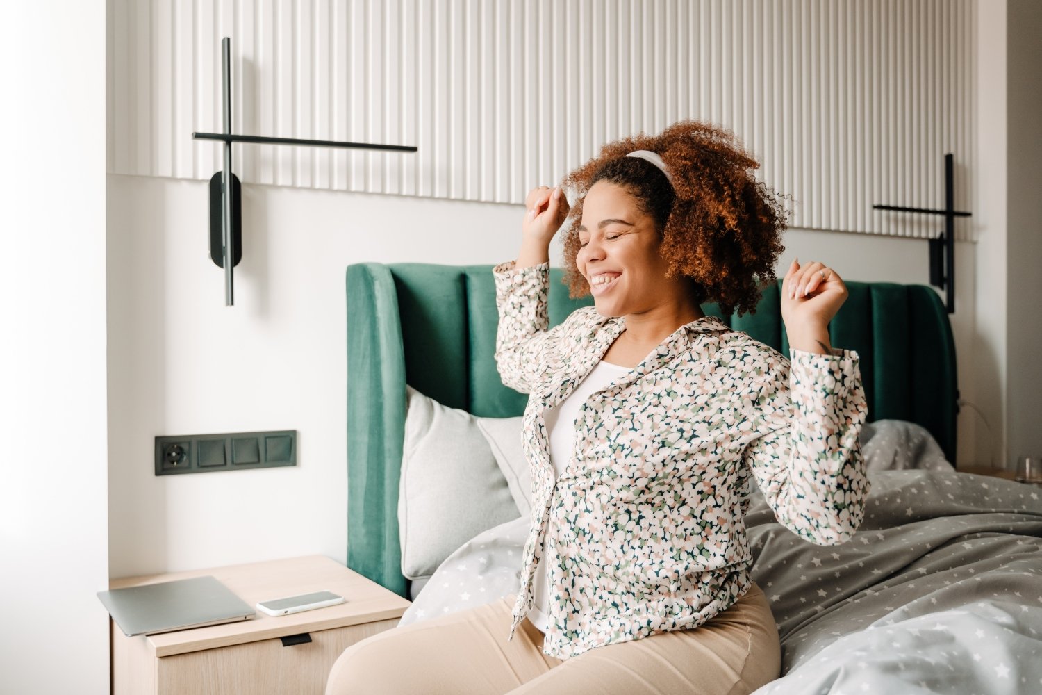 Young beautiful smiling african woman sitting on bed and stretching