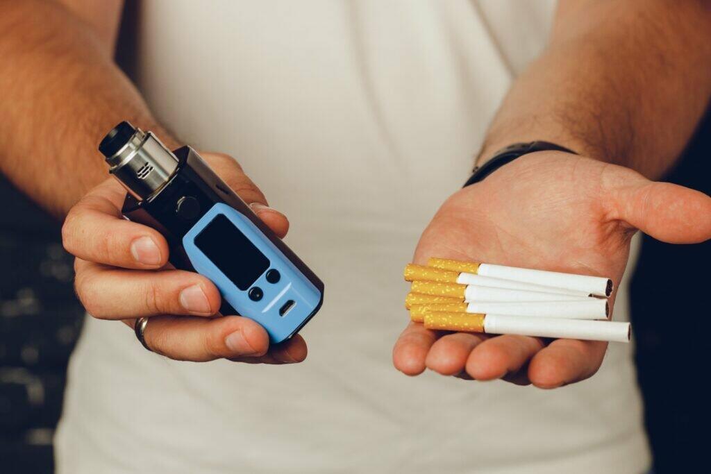 Male holding cigarettes and vape inhaler close up photo