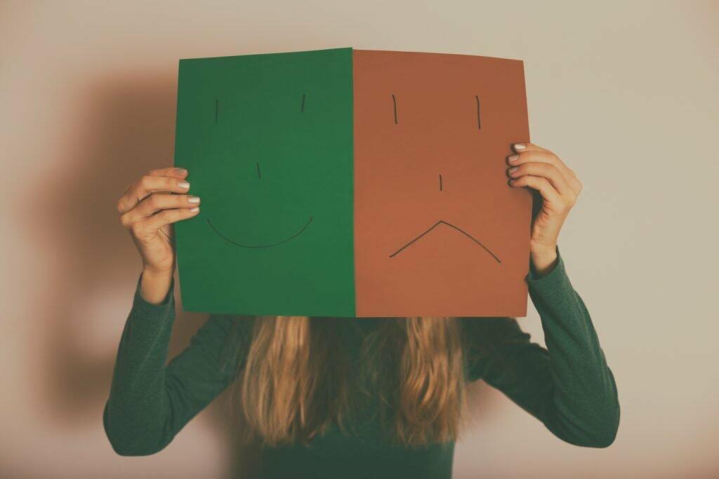 image of a woman holding out papers with a sad and smiling face drawn on them. sad and happy emotions concept
