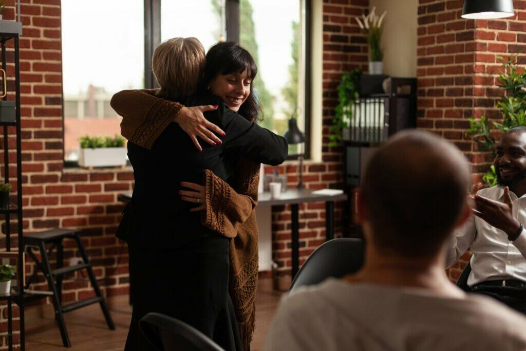 Woman and therapist hugging after sharing recovery progress with aa meeting group