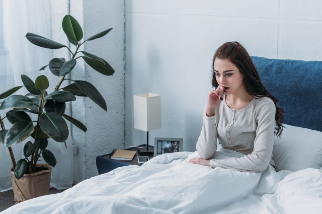 beautiful depressed woman lying in bed and biting finger