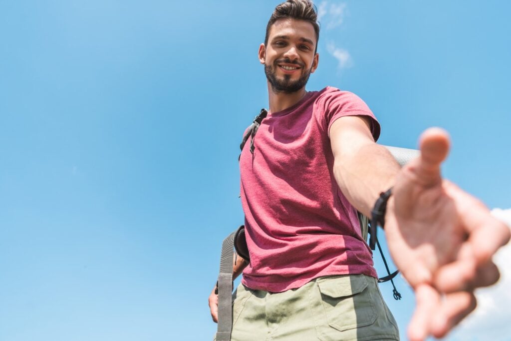 bottom view of handsome young tourist stretching out hand, blue sky on background