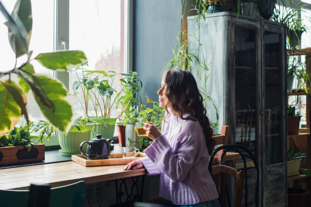 woman drinking tea at home surrounded with house plants